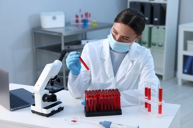 Laboratory testing. Doctor holding test tube with blood sample at table indoors