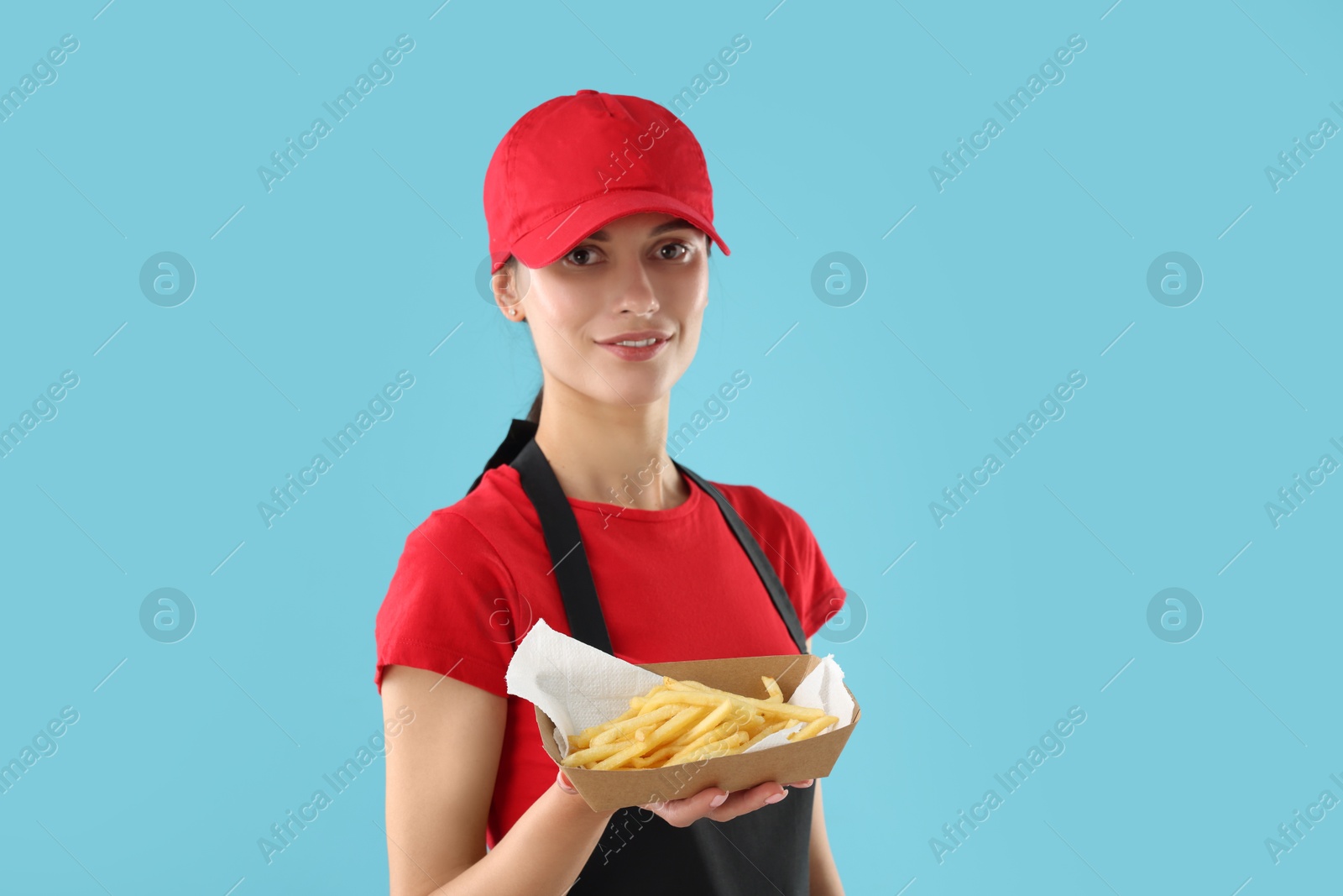 Photo of Fast-food worker holding paper container with fries on light blue background