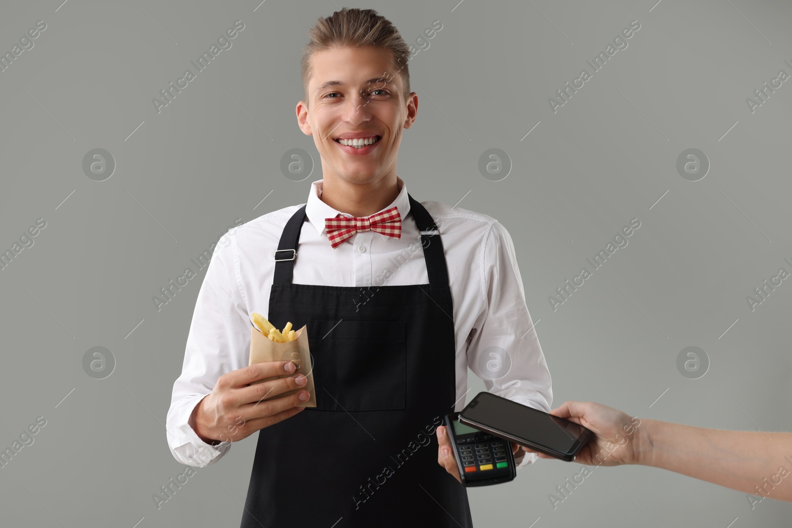 Photo of Fast-food worker taking payment from client via terminal on gray background, closeup