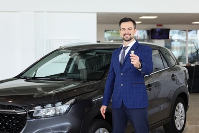 Photo of Happy salesman holding key near new black car in salon