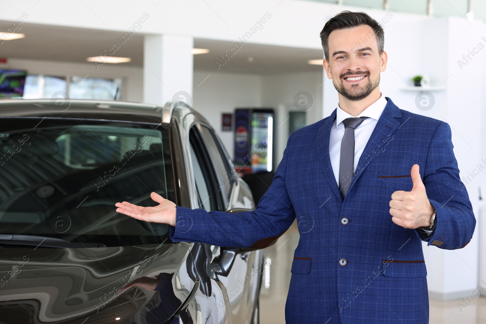 Photo of Happy salesman showing thumbs up near new black car in salon