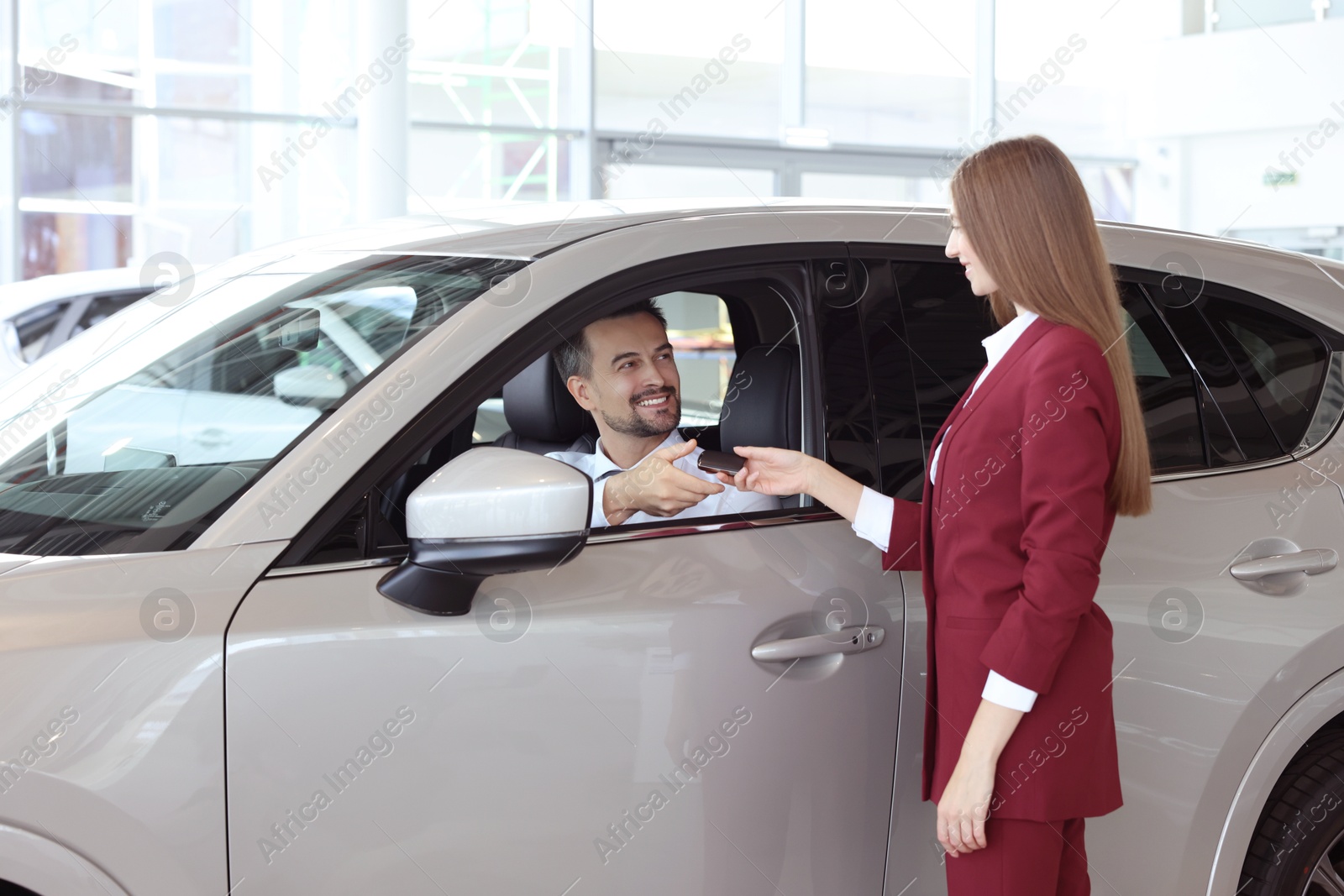 Photo of Happy saleswoman and client inside new silver car in salon