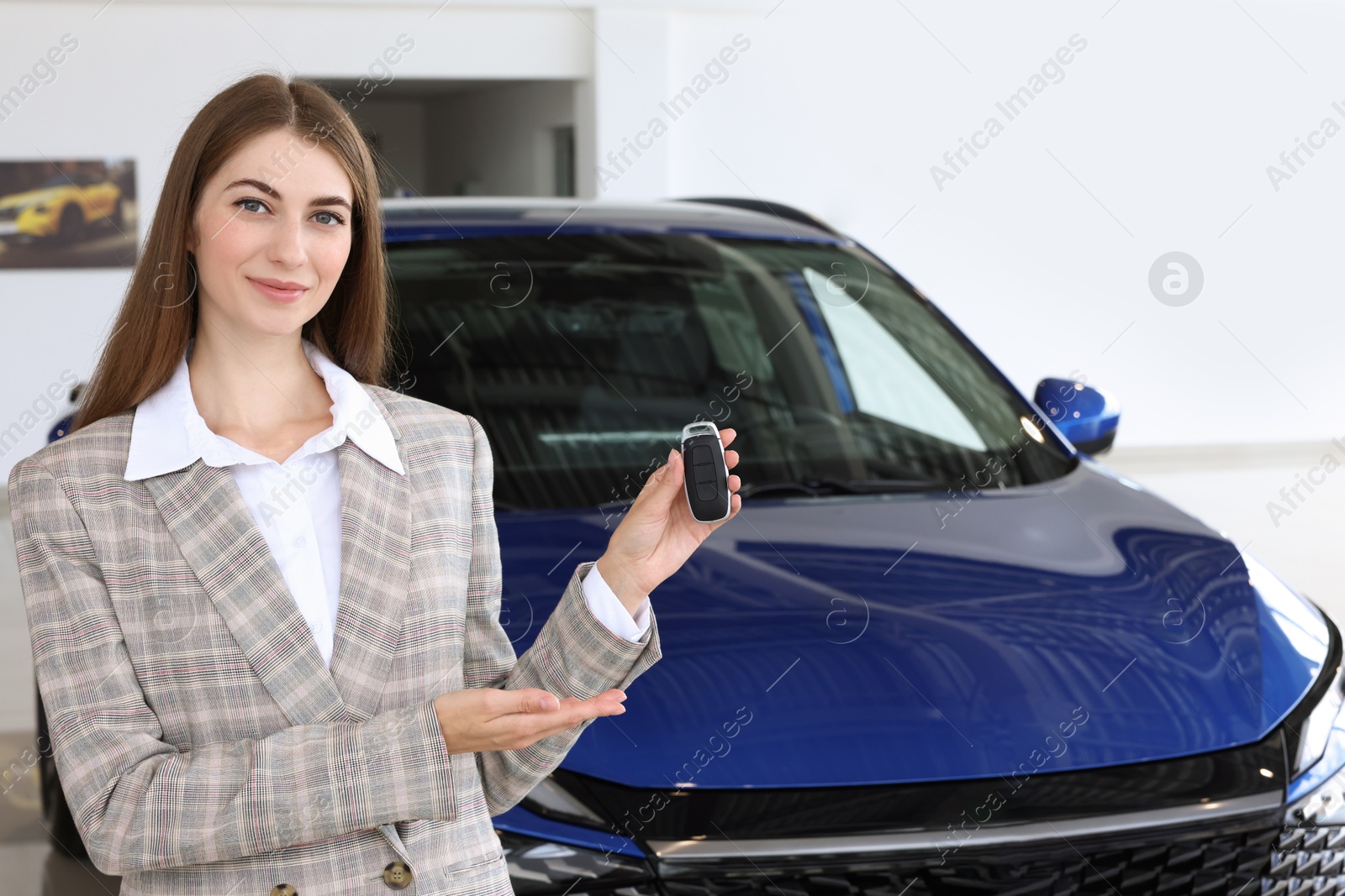 Photo of Happy saleswoman holding key near new car in salon