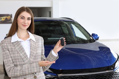 Photo of Happy saleswoman holding key near new car in salon