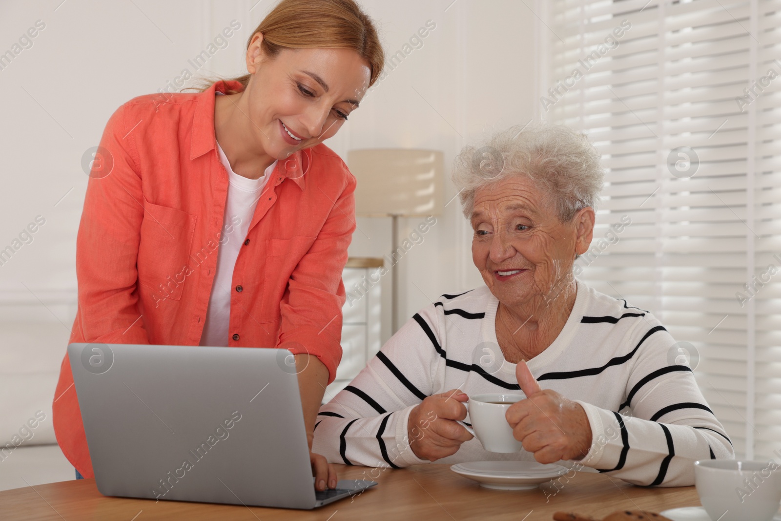 Photo of Caregiver showing something on laptop to senior woman at home