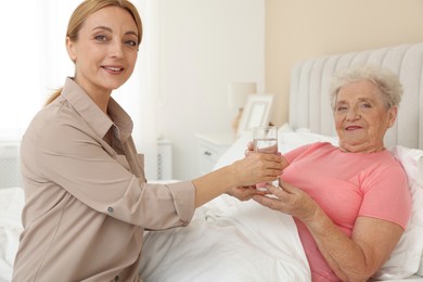 Photo of Caregiver giving glass of water to senior woman at home