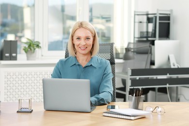 Photo of Portrait of smiling middle aged woman at table in office