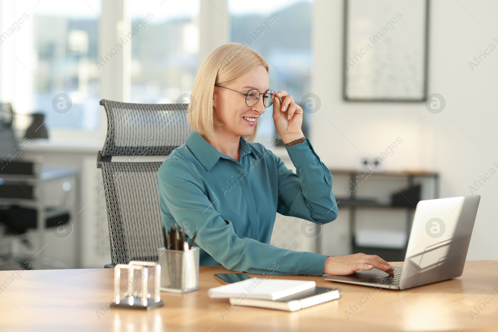 Photo of Smiling middle aged woman working with laptop at table in office