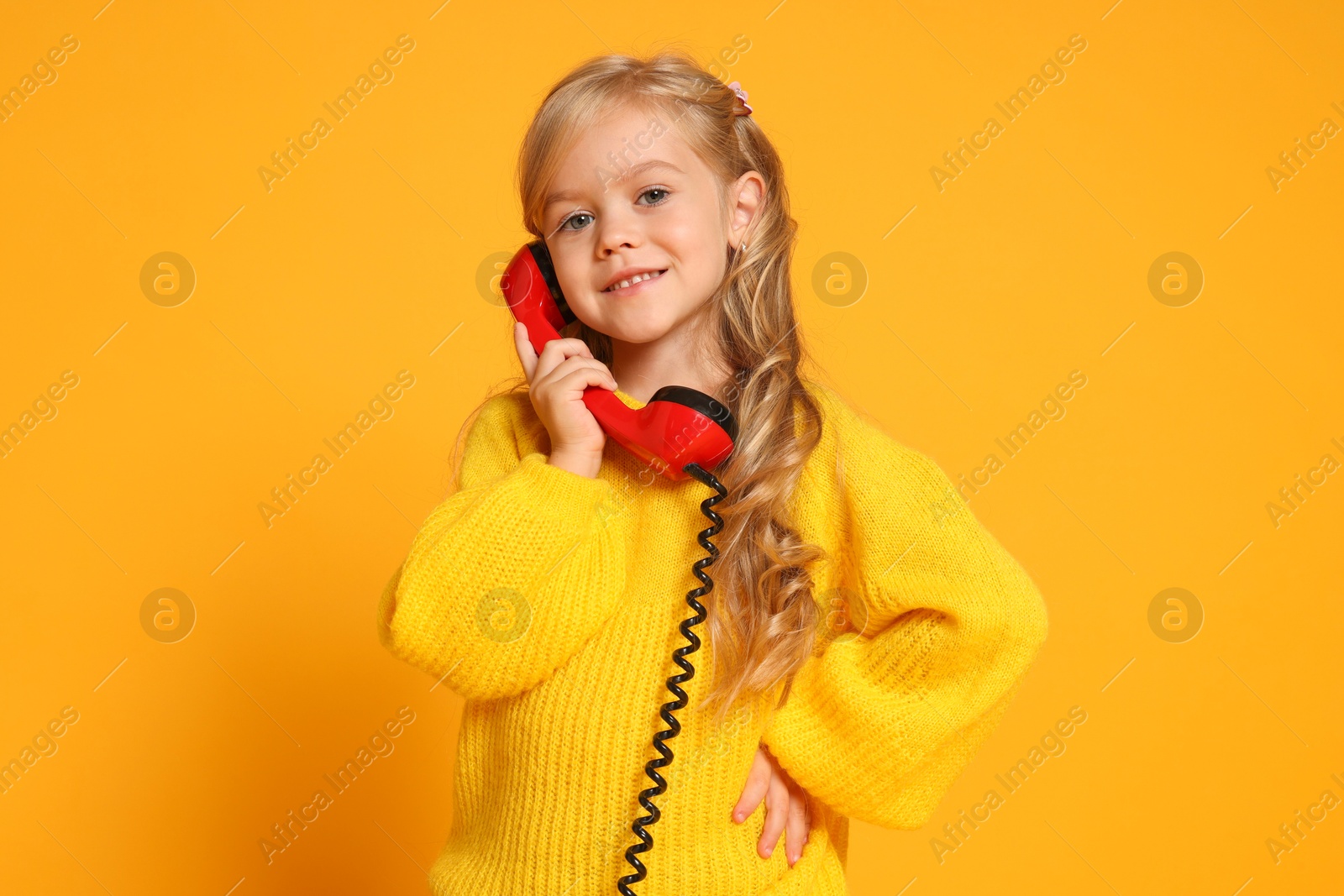 Photo of Cute little girl with handset of telephone on orange background