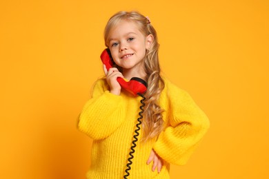 Photo of Cute little girl with handset of telephone on orange background