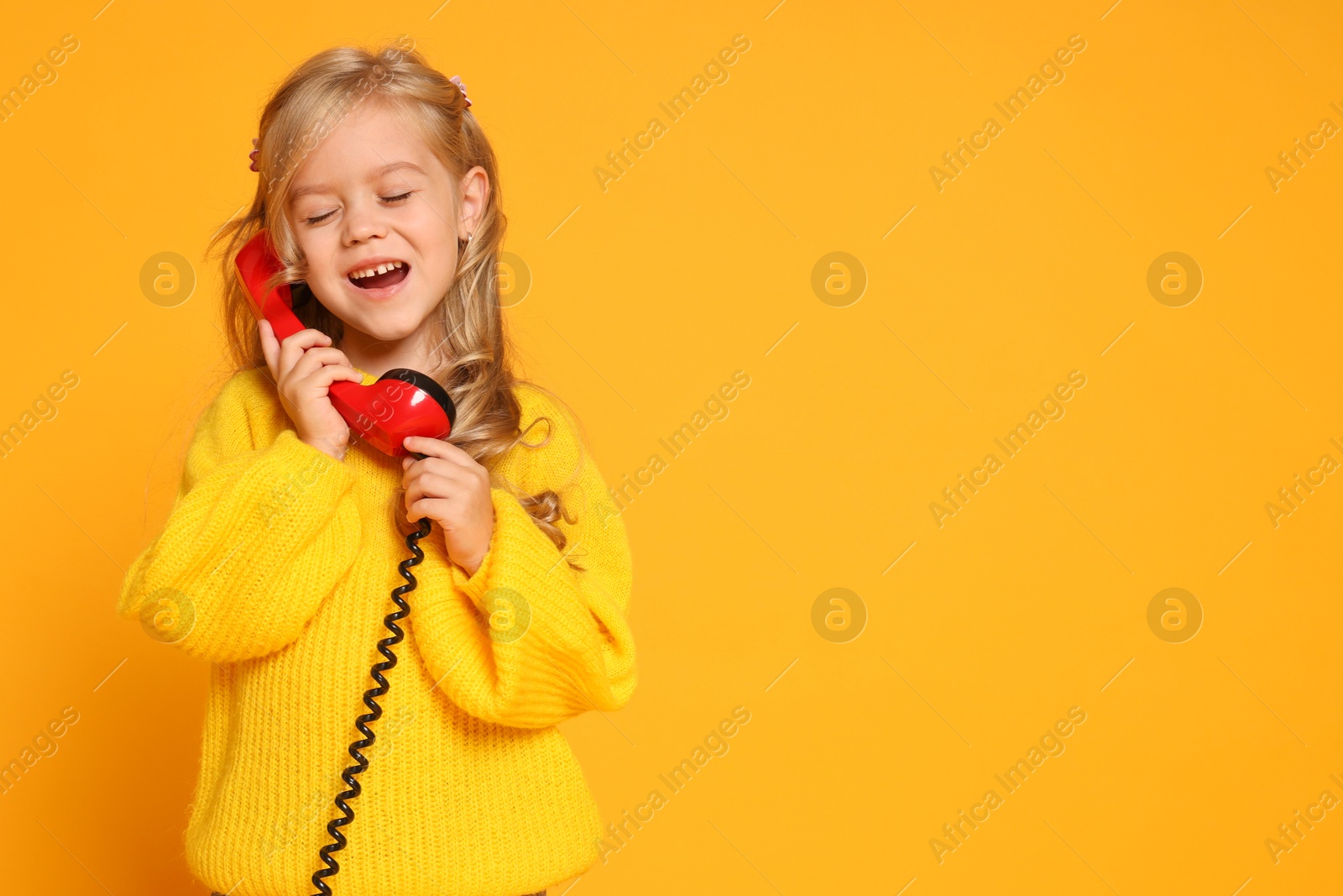 Photo of Cute little girl with handset of telephone on orange background, space for text