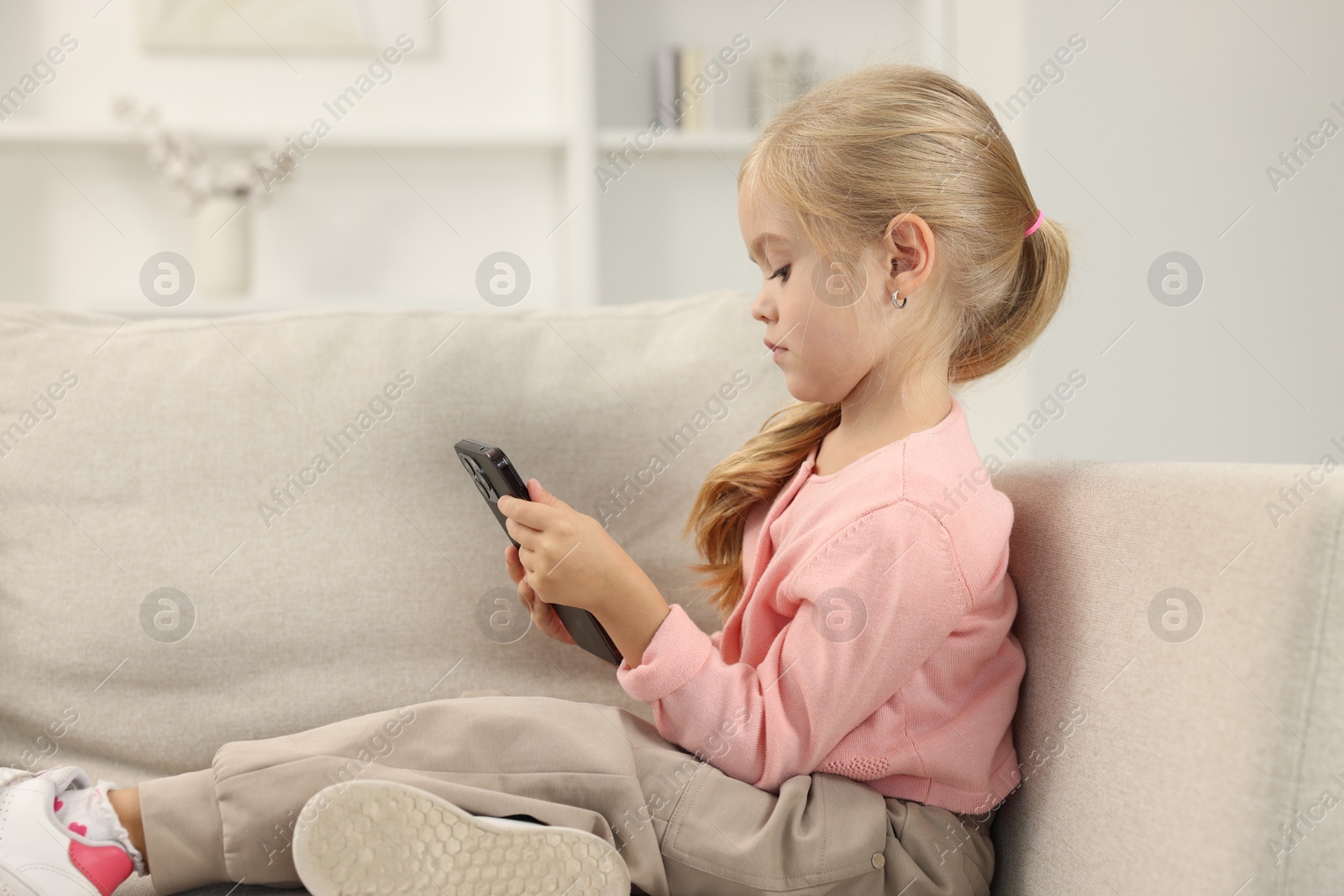 Photo of Cute little girl using smartphone on sofa at home