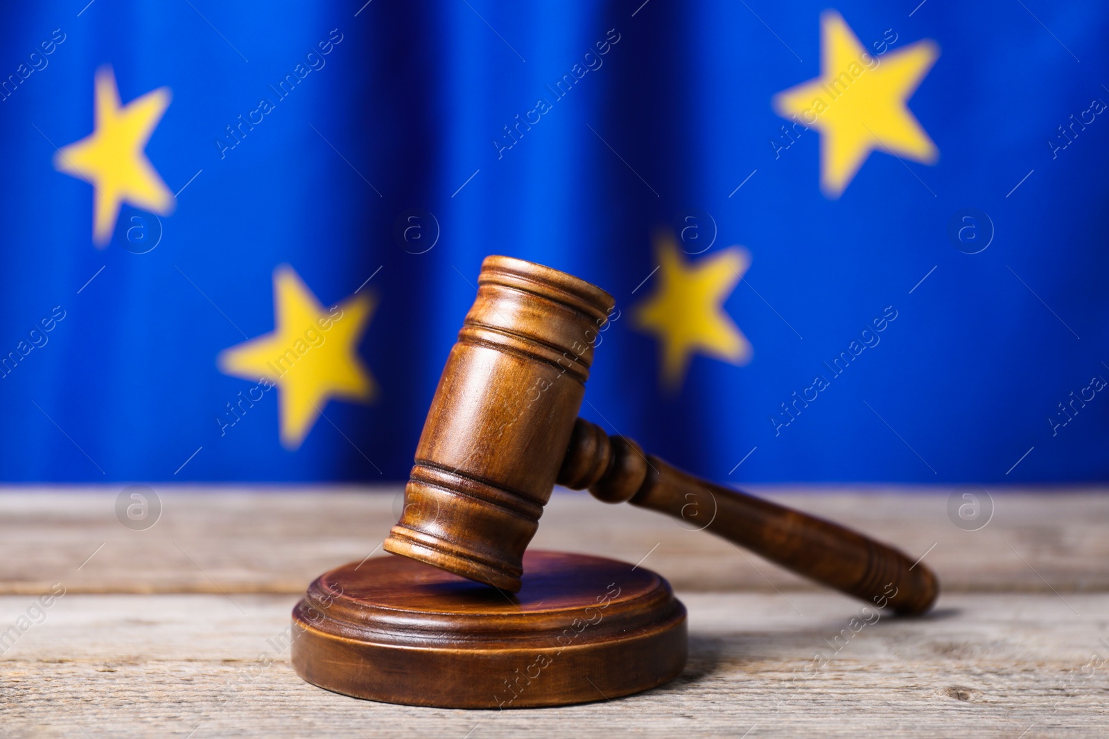 Photo of Judge's gavel on wooden table against European Union flag, closeup