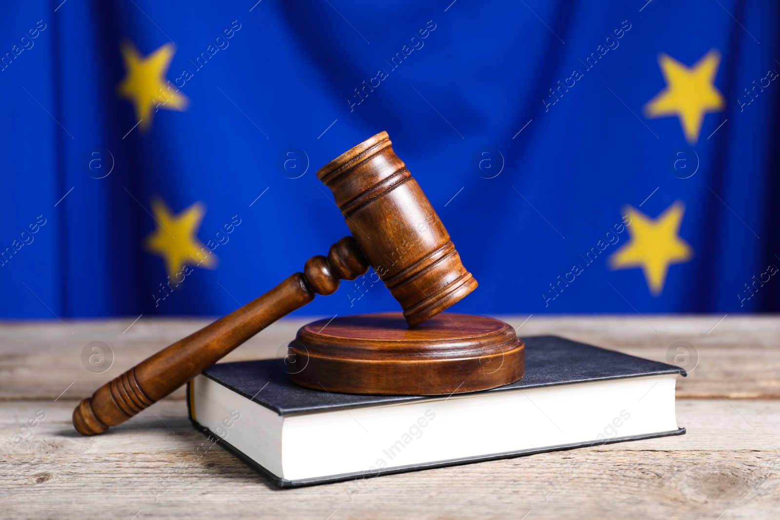 Photo of Judge's gavel and book on wooden table against European Union flag, closeup