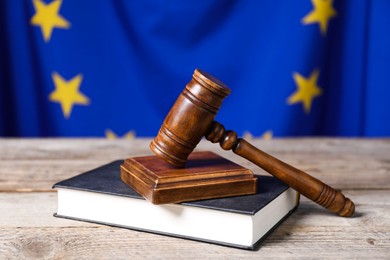 Judge's gavel and book on wooden table against European Union flag, closeup