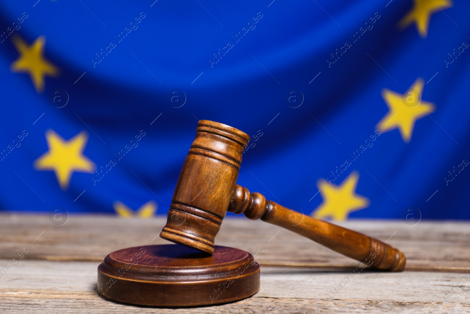 Photo of Judge's gavel on wooden table against European Union flag, closeup