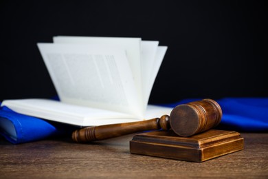 Photo of Judge's gavel, open book and European Union flag on wooden table against black background, closeup