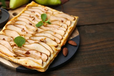 Photo of Delicious puff pastry tart with pears, almond and mint on wooden table, closeup. Space for text