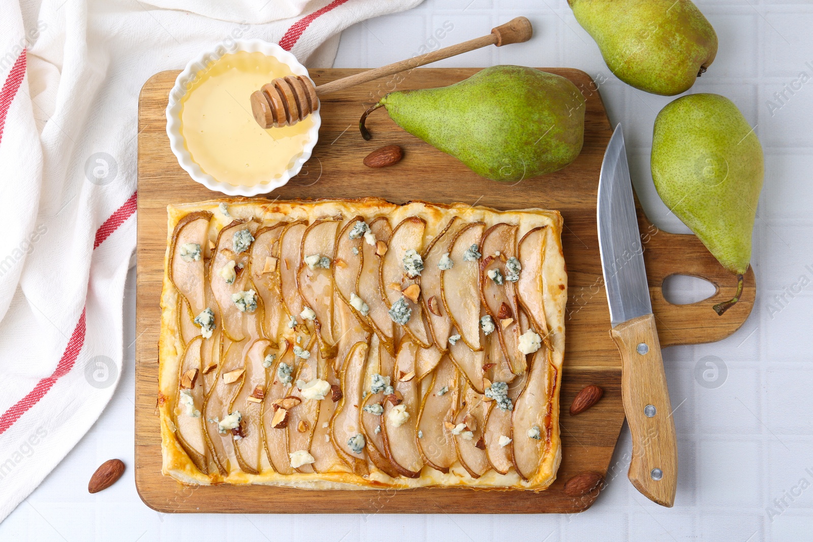 Photo of Delicious puff pastry tart with pears, almond, honey and blue cheese on light tiled table, flat lay