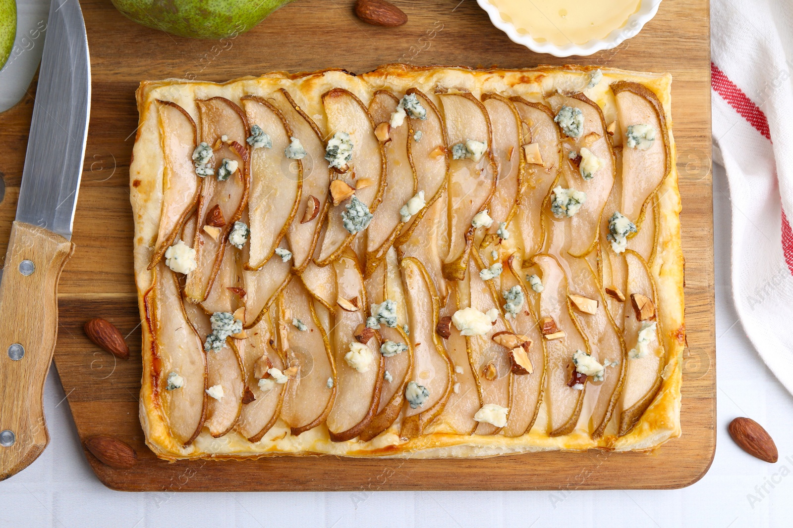 Photo of Delicious puff pastry tart with pears, almond, honey and blue cheese on light tiled table, flat lay