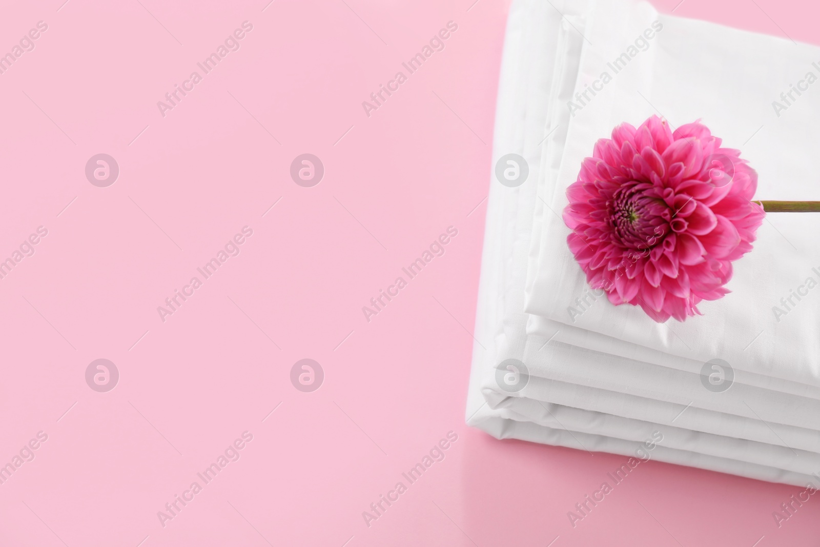 Photo of Stacked clean bed linens and flower on pink background, top view. Space for text