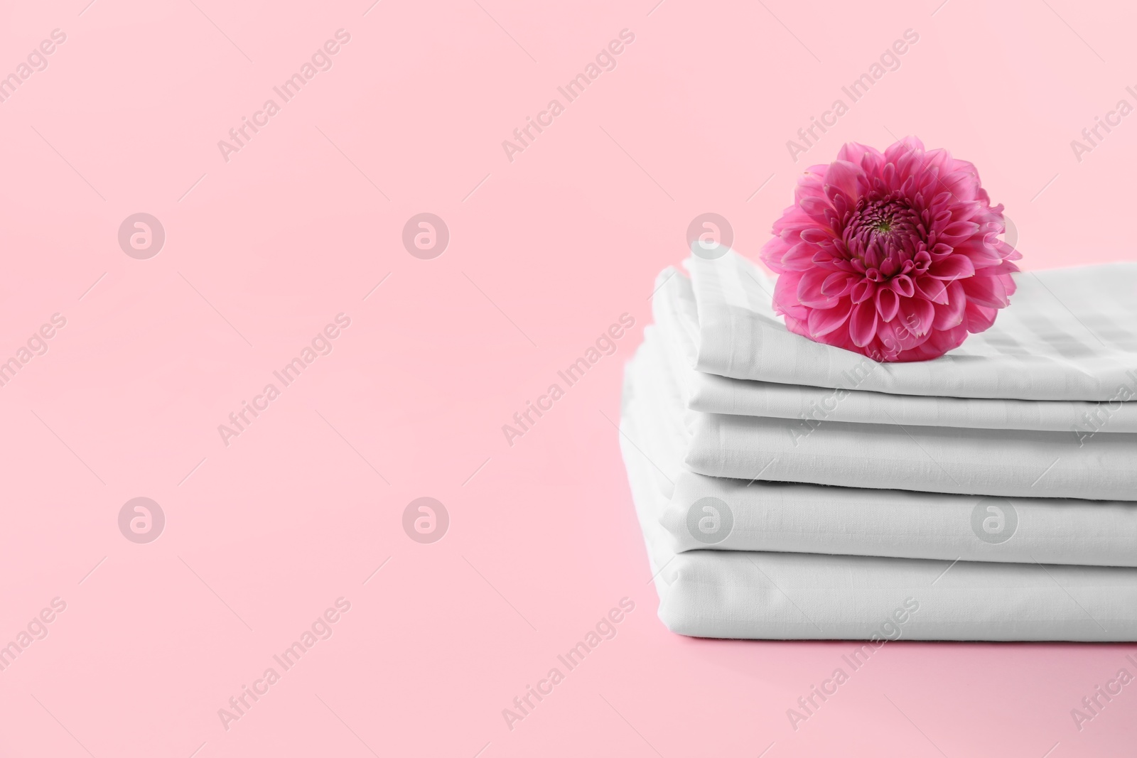 Photo of Stacked clean bed linens and flower on pink background, space for text