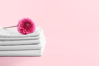 Photo of Stacked clean bed linens and flower on pink background, space for text