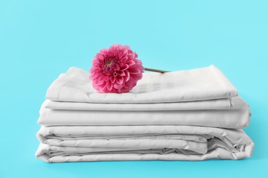 Photo of Stacked clean bed linens and pink flower on light blue background