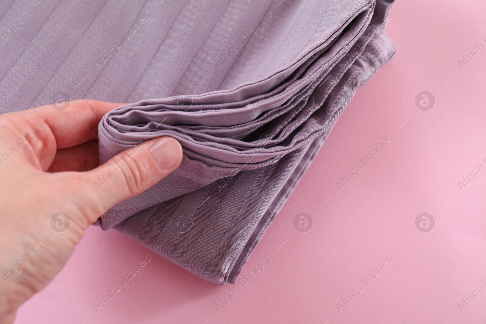 Photo of Woman with stacked bed linens on pink background, closeup