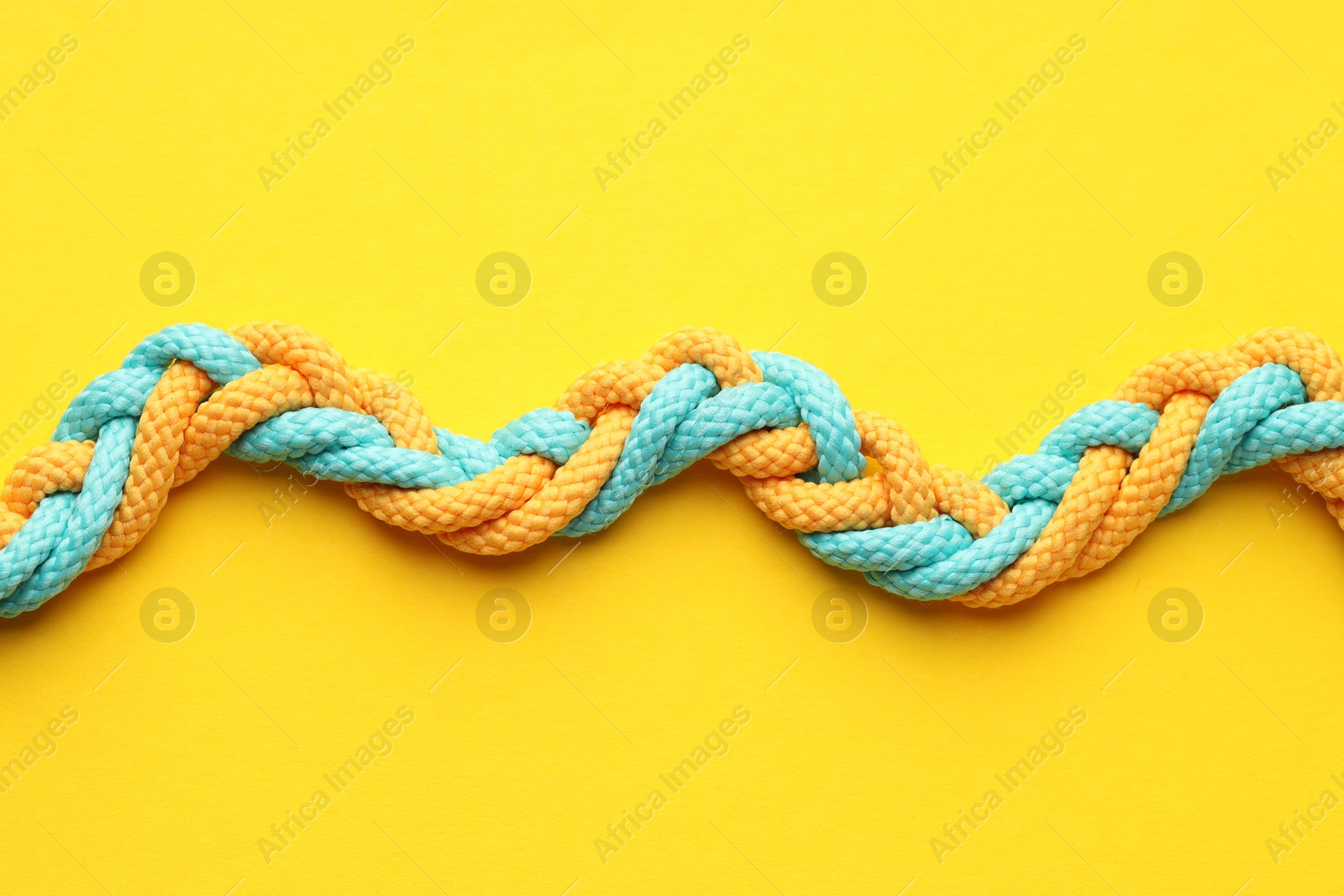 Photo of Colorful ropes tied together on yellow background, top view. Unity concept