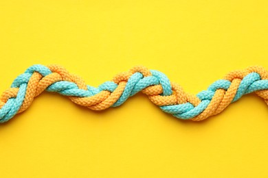 Photo of Colorful ropes tied together on yellow background, top view. Unity concept