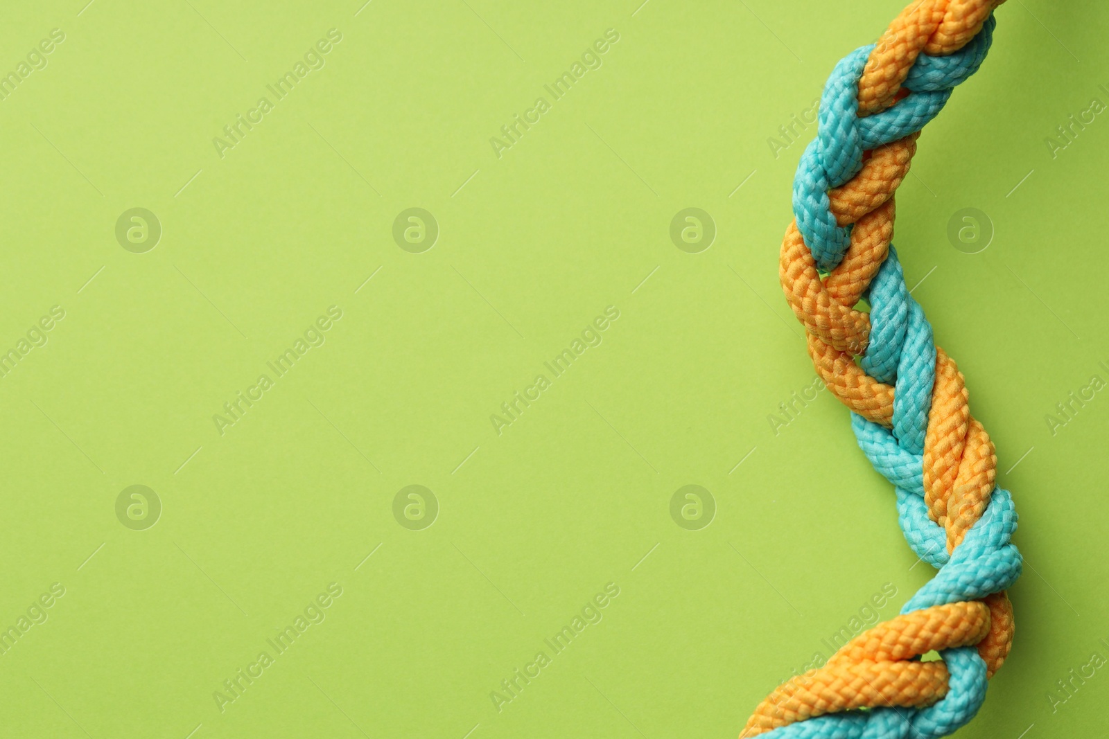 Photo of Colorful ropes tied together on light green background, top view and space for text. Unity concept