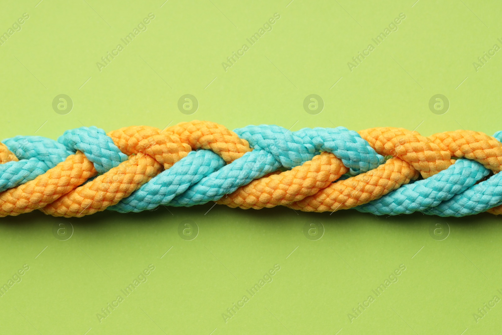 Photo of Colorful ropes tied together on light green background, top view. Unity concept