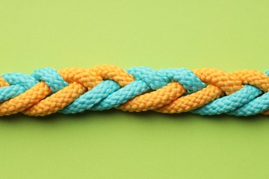 Photo of Colorful ropes tied together on light green background, top view. Unity concept