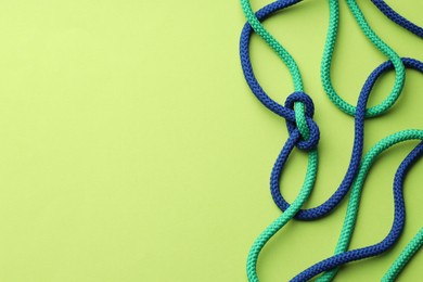 Photo of Colorful ropes tied in knot on light green background, top view and space for text. Unity concept