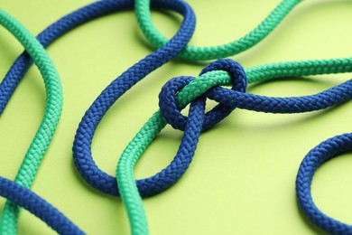 Colorful ropes tied in knot on light green background, closeup. Unity concept