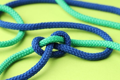 Colorful ropes tied in knot on light green background, closeup. Unity concept