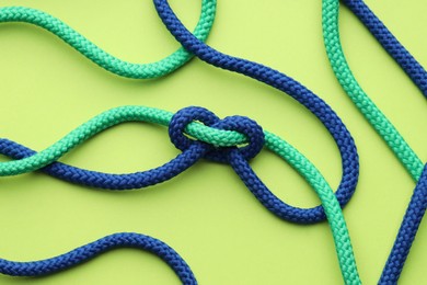 Colorful ropes tied in knot on light green background, top view. Unity concept