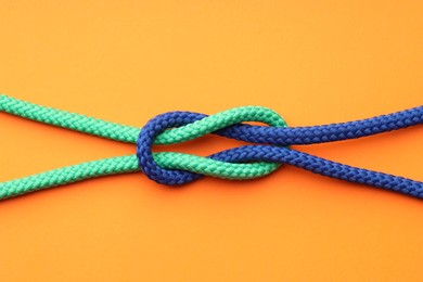 Colorful ropes tied in knot on orange background, top view. Unity concept