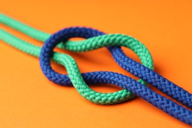 Colorful ropes tied in knot on orange background, closeup. Unity concept