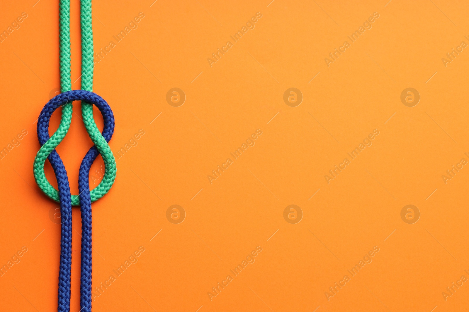 Photo of Colorful ropes tied in knot on orange background, top view and space for text. Unity concept