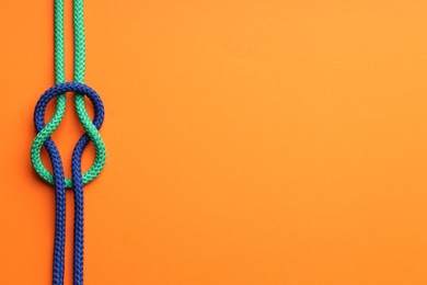 Photo of Colorful ropes tied in knot on orange background, top view and space for text. Unity concept