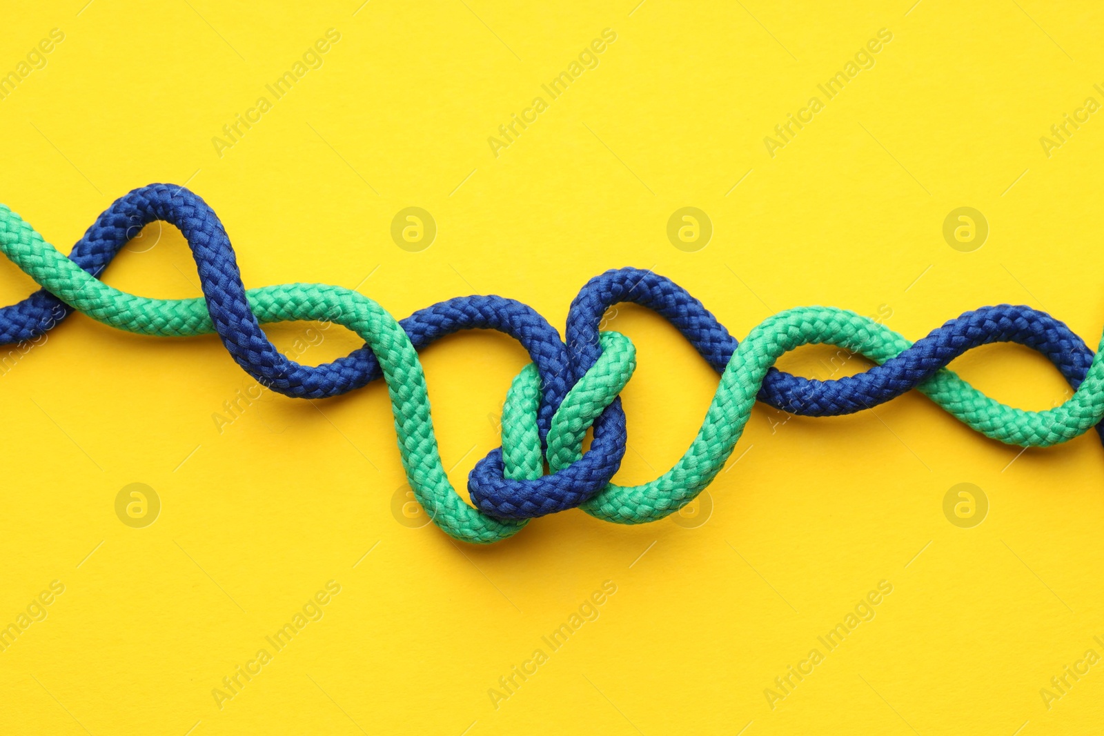 Photo of Colorful ropes tied in knot on yellow background, top view. Unity concept