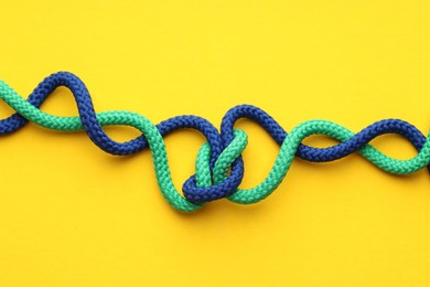 Photo of Colorful ropes tied in knot on yellow background, top view. Unity concept