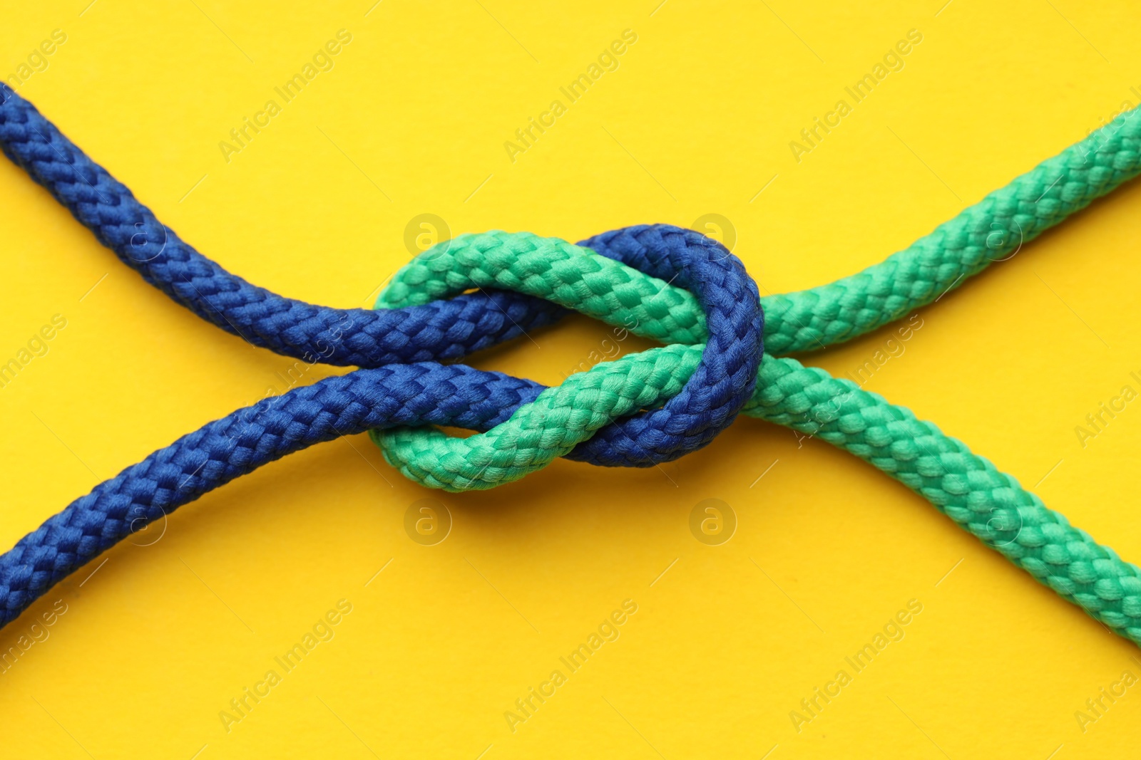 Photo of Colorful ropes tied in knot on yellow background, top view. Unity concept