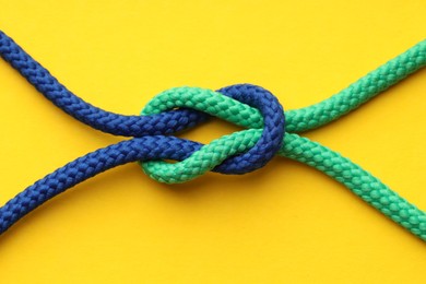 Photo of Colorful ropes tied in knot on yellow background, top view. Unity concept