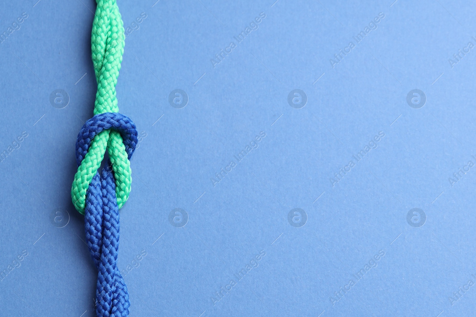 Photo of Colorful ropes tied in knot on blue background, top view and space for text. Unity concept