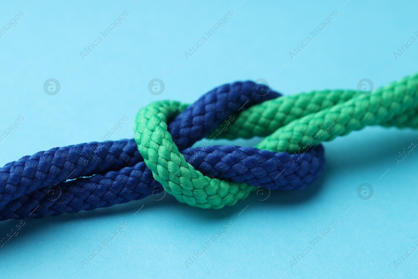 Photo of Colorful ropes tied in knot on light blue background, closeup. Unity concept