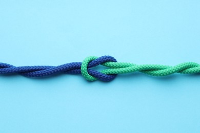 Photo of Colorful ropes tied in knot on light blue background, top view. Unity concept