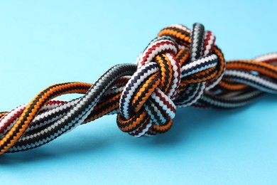 Photo of Colorful ropes tied in knot on light blue background, closeup. Unity concept